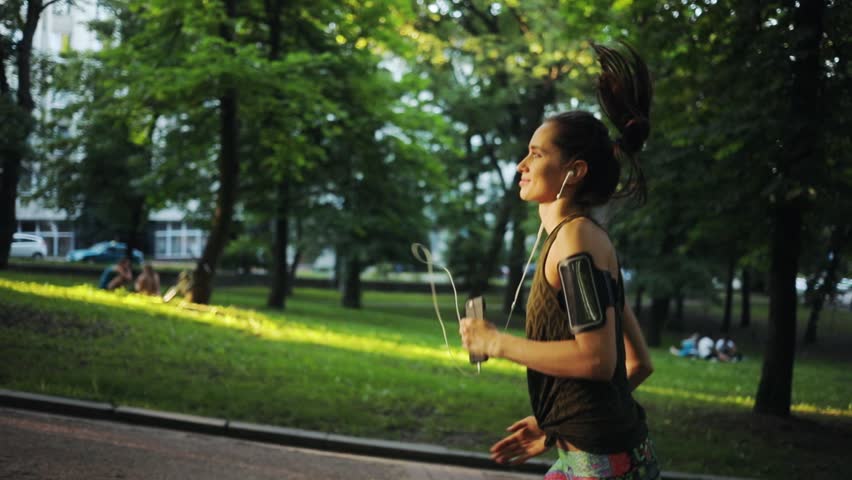 Beautiful Runner Woman Running In Park Exercising Outdoors Fitness Tracker Slow Motion Sunlight Healthy Young Jogging Music Sport Girl Summer Nature Technology Active Athlete Workout Sunset Body
