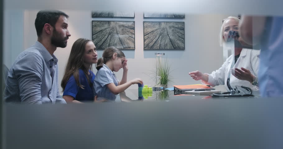 Slow Motion Shot Of A Doctor Or Specialist Having Conversation In Clinic With Parents About Their Autistic Girls Health Doctor In Hospital Show Little Girl With Aspergers Lab Test Results To Parents