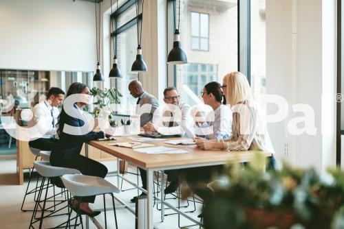 Smiling Group Of Diverse Businesspeople Discussing Paperwork Together While Having A Meeting Around A Table In A Modern Office